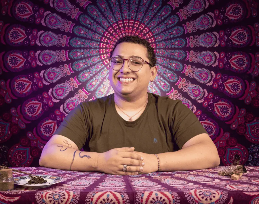 Victor Augusto sorrindo, sentado à mesa diante de uma mandala colorida